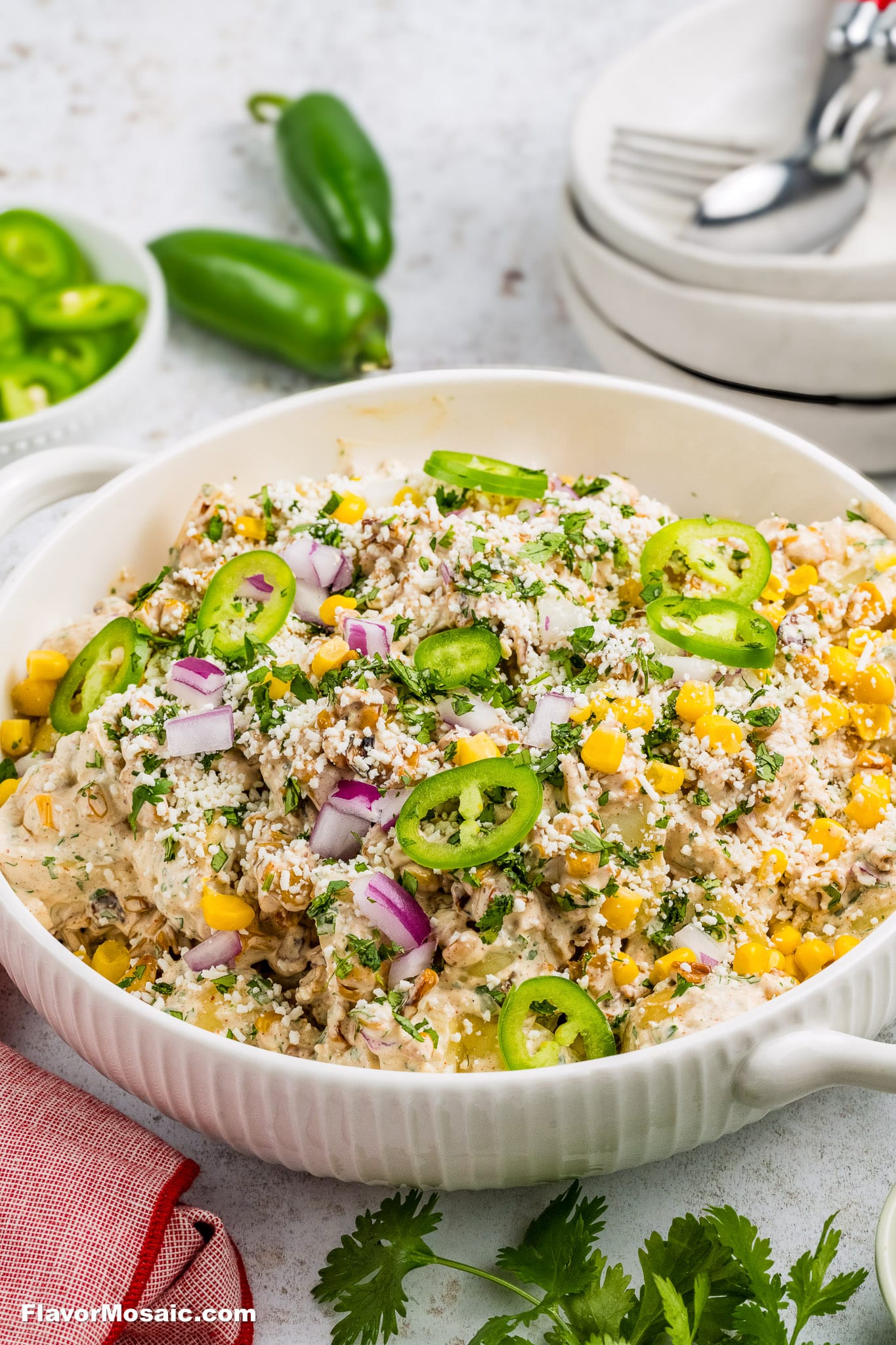 Mexican Street Corn Salad in a white bowl with sliced jalapeños on top and whole jalapeños in the background.