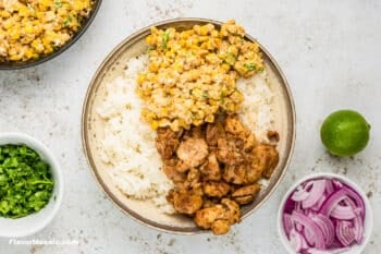 A large bowl with cooked rice, with corn, and seasoned chicken layered on top.