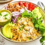 View on finished Street Corn Chicken Rice Bowl topped with sliced avocado, cilantro leaves, sliced red onions and a small bowl of sauce.