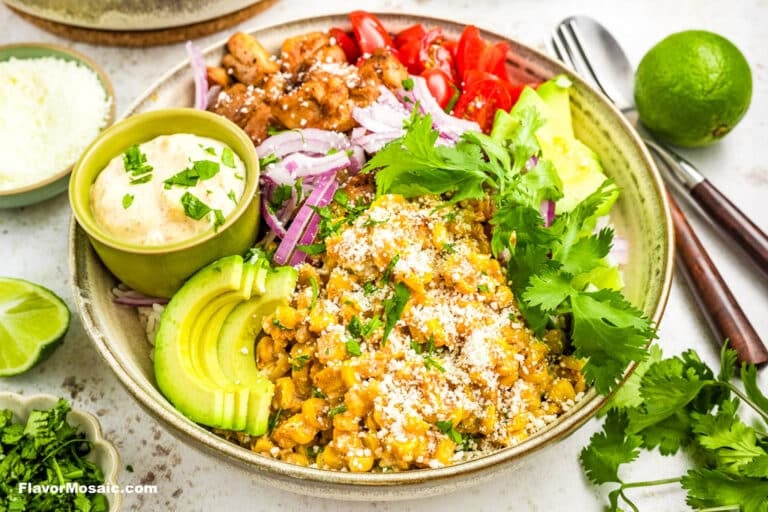 View on finished Street Corn Chicken Rice Bowl topped with sliced avocado, cilantro leaves, sliced red onions and a small bowl of sauce.