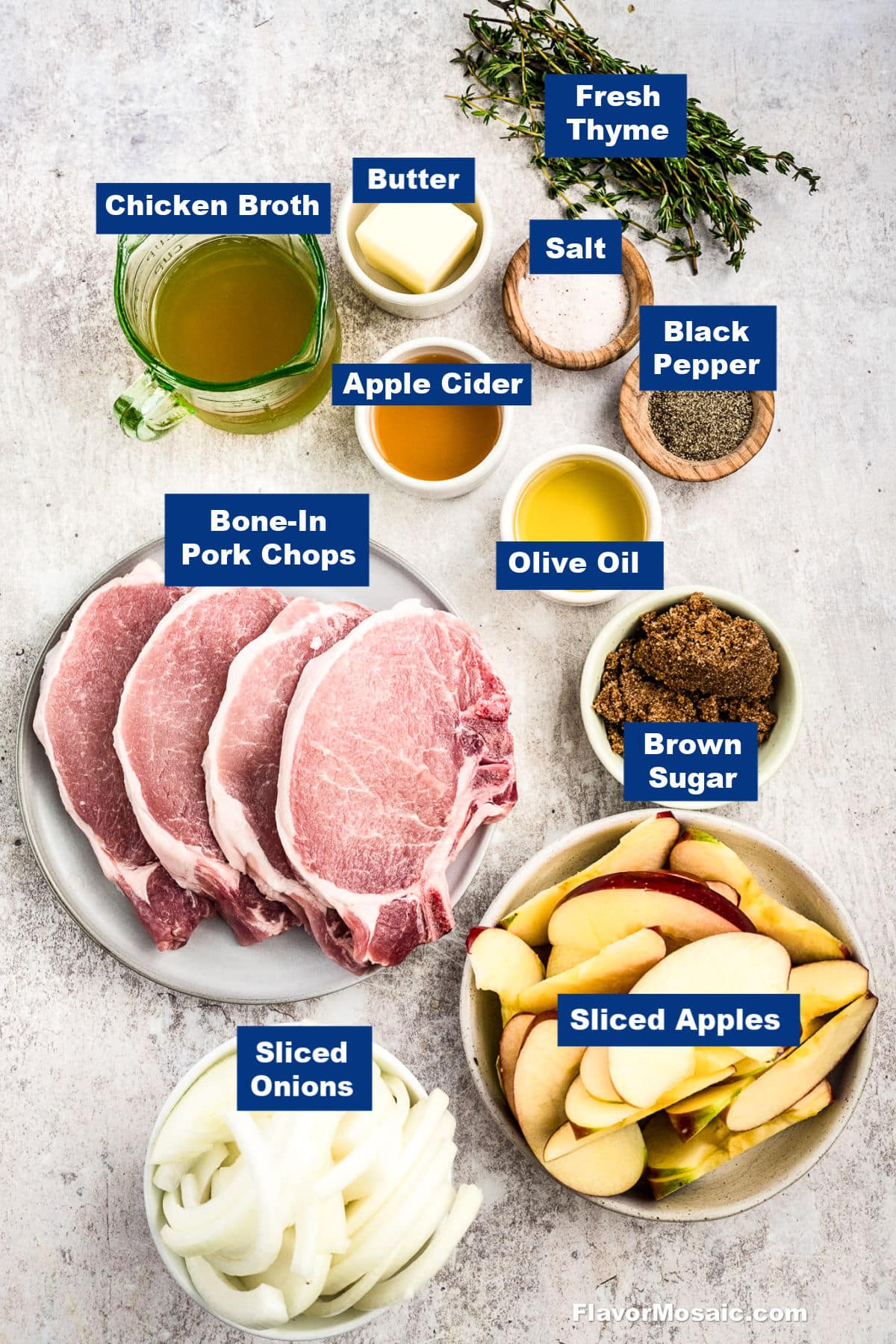 Overhead view of ingredients for a pork chop recipe, including bone-in pork chops, sliced apples, sliced onions, brown sugar, olive oil, apple cider, chicken broth, butter, fresh thyme, salt, and black pepper, all labeled.