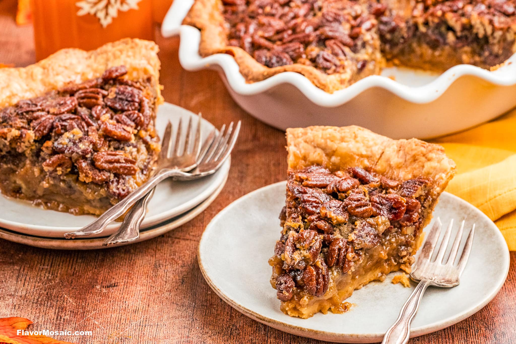 Two slices of Texas Pecan Pie on small plates with forks sit on a wooden table. The pies have golden crusts and crunchy pecan topping, with the remaining pie in a white pie dish in the background.