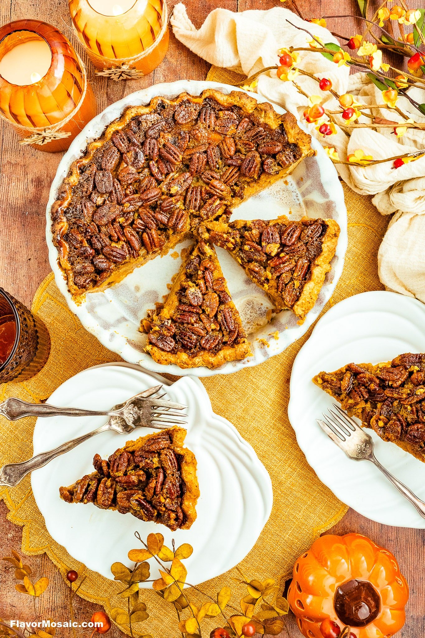 A pecan pie with one slice missing sits on a table alongside two plated slices, autumn decorations, candles, and a small pumpkin, evoking a cozy fall or Thanksgiving setting.