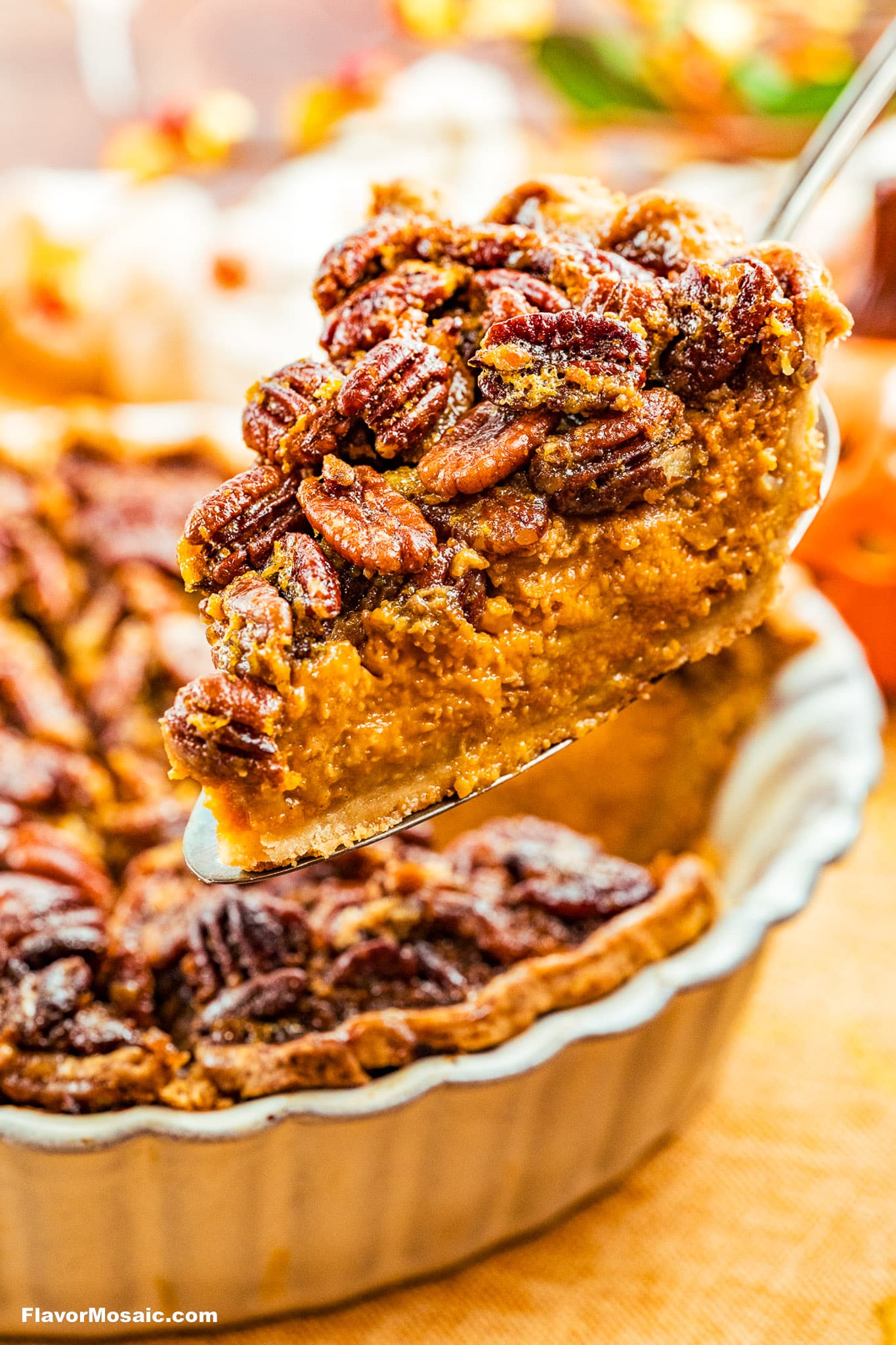 A close-up of a slice of pecan pie being lifted from a pie dish, showing a golden, nutty topping and a rich, moist filling, with autumn-themed decorations blurred in the background.