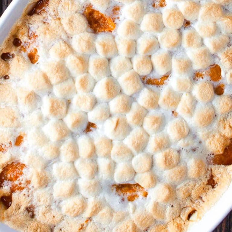 A baked casserole topped with a layer of melted, golden-brown mini marshmallows, with hints of caramelized filling showing through.