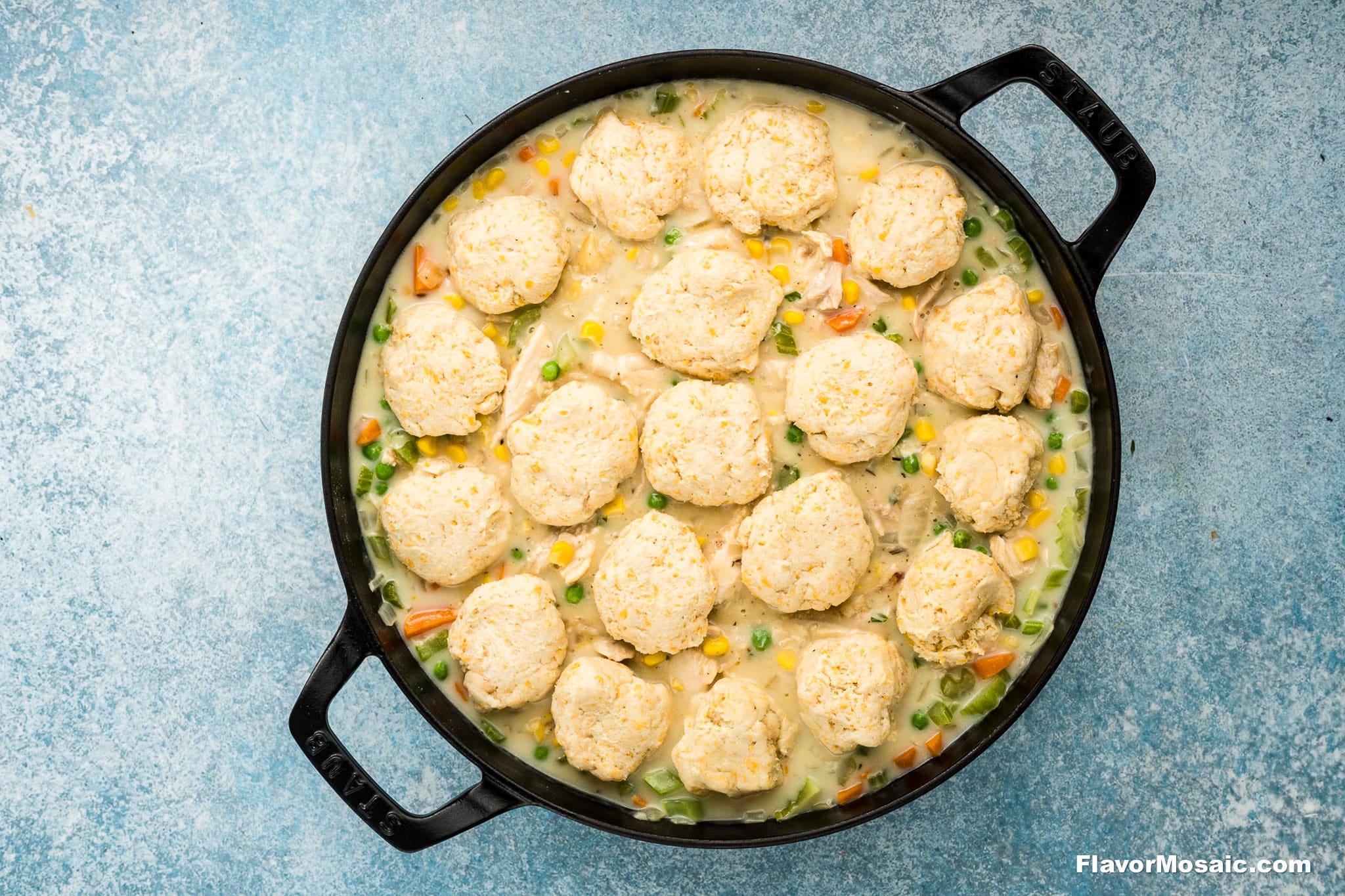 A black cast iron skillet filled with creamy Cheddar Bay Biscuit Chicken Pot Pie, topped with golden, round biscuits, sits on a light blue textured surface.