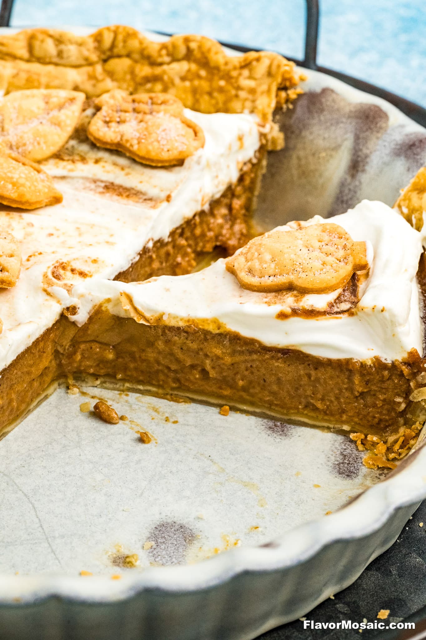A close-up of a partially sliced Apple Butter Pie topped with whipped cream and decorative pie crust shapes, in a white ceramic pie dish.