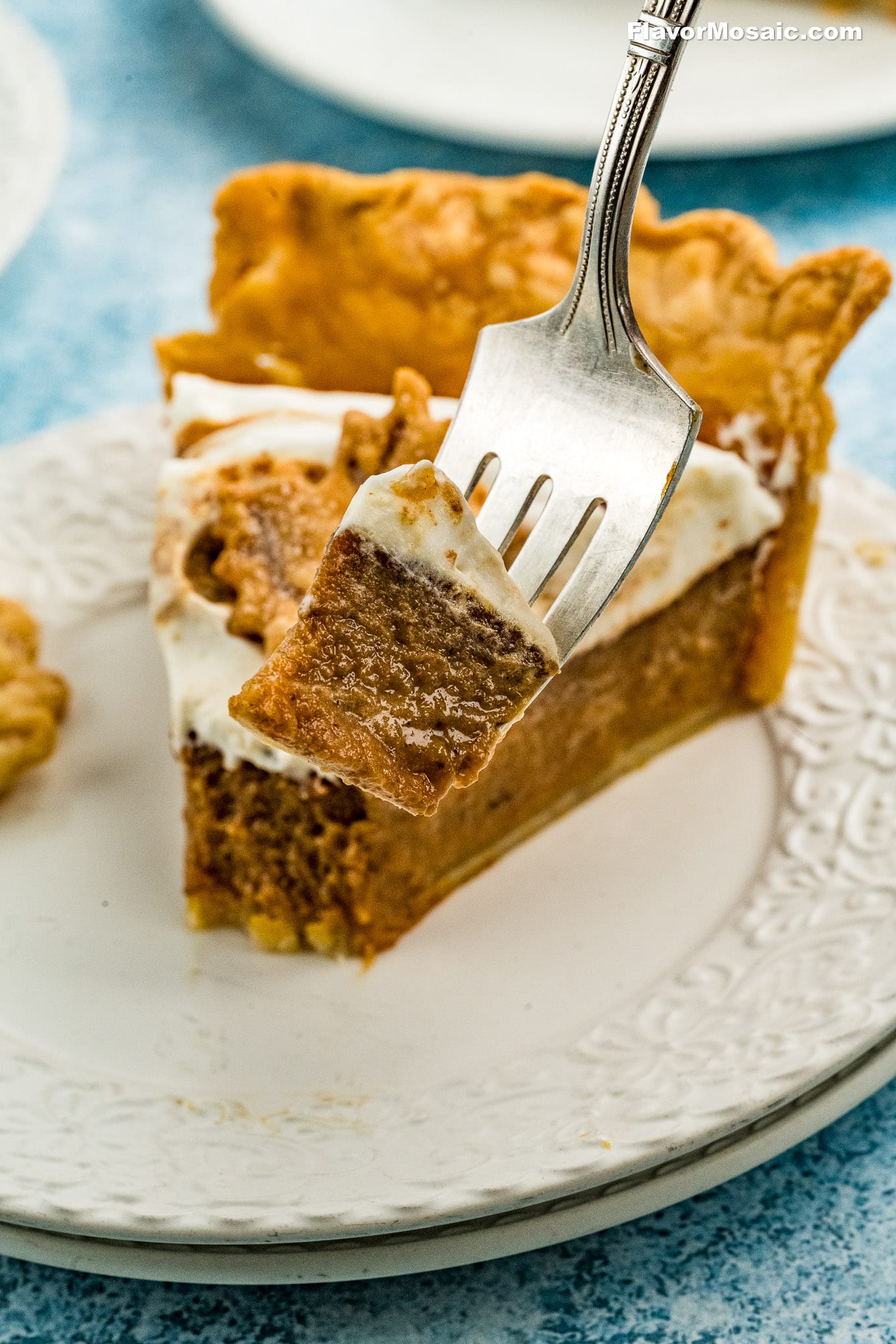 A close-up of a fork holding a bite of creamy Apple Butter Pie with a golden crust, above a slice of pie on a white decorative plate.