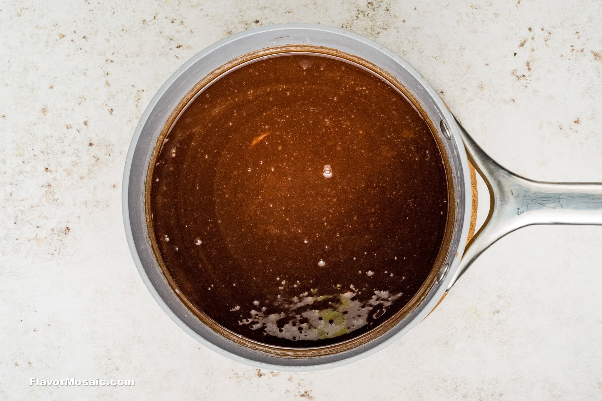 A top-down view of a saucepan filled with a smooth, glossy Chocolate Chess Pie mixture on a light, textured surface. The handle is visible on the right side.