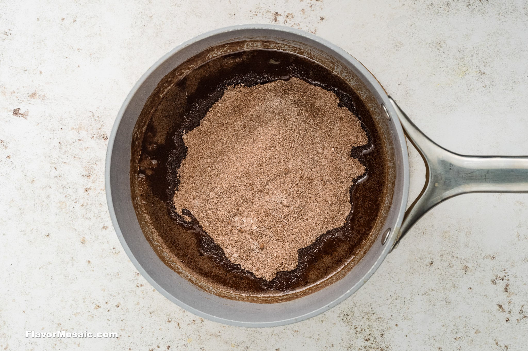 Step 6 - Dry ingredients whisked with the chocolate-egg mixture in a silver saucepan on a light colored background