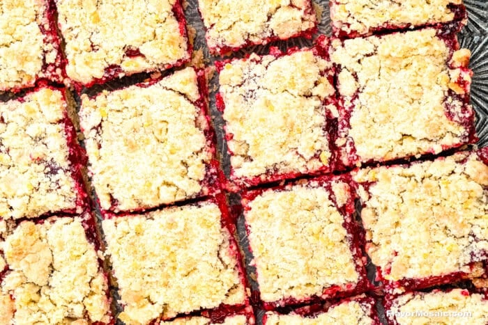 A close-up view of several cranberry crumb bars cut into squares, showing a vibrant red cherry filling and a golden, crumbly topping.