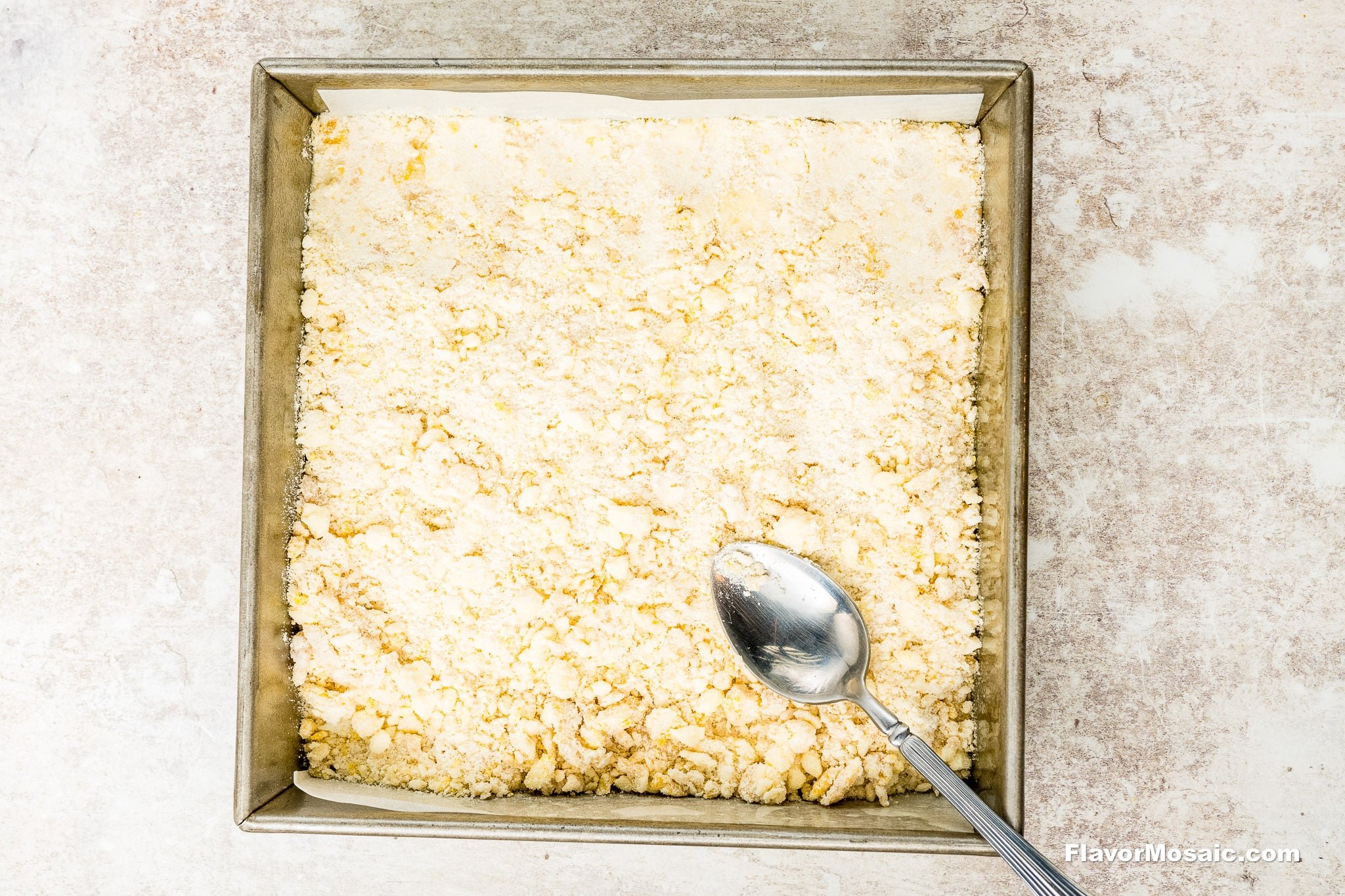 A square baking pan filled with an even layer of crumbly, pale yellow mixture-perfect for making Cranberry Bars-with a metal spoon resting on top, ready to serve these delicious cranberry crumb bars.