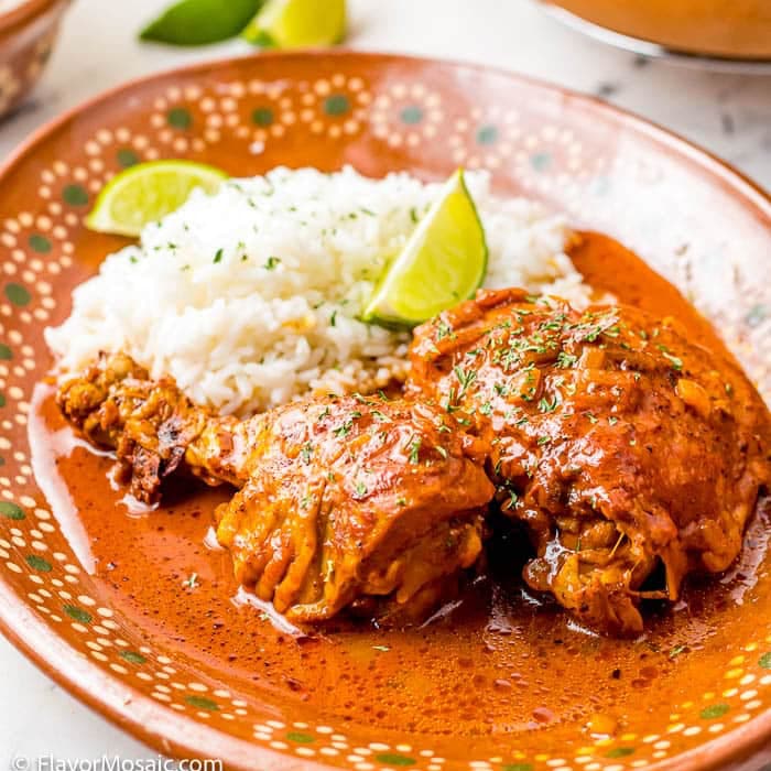 A decorative plate with two pieces of saucy chicken in red sauce, garnished with herbs and lime wedges, served alongside white rice-a delicious nod to Southern & Tex-Mex Instant Pot Comfort Food Recipes.
