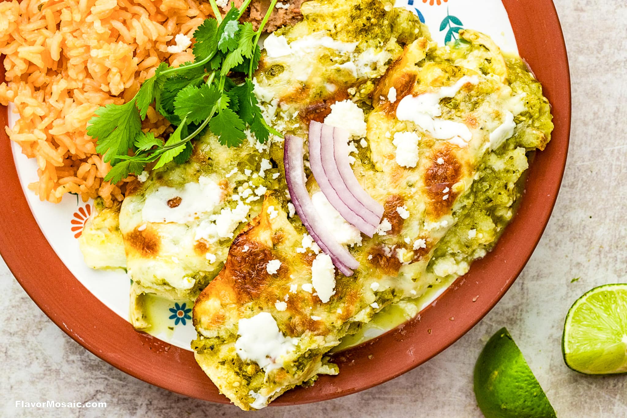 A plate of cheesy enchiladas verdes topped with sliced red onion, crema, cilantro, and queso fresco, served alongside orange Mexican rice. Lime wedges are on the side.