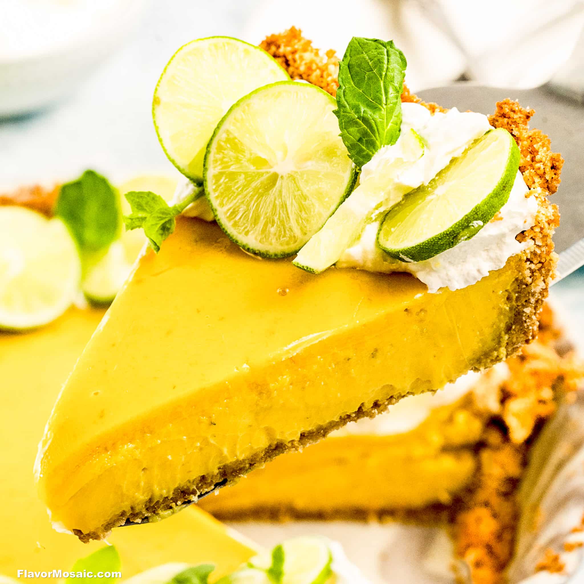 A slice of classic Key Lime Pie with a graham cracker crust, topped with whipped cream, fresh lime slices, and mint leaves is being lifted from the whole pie.