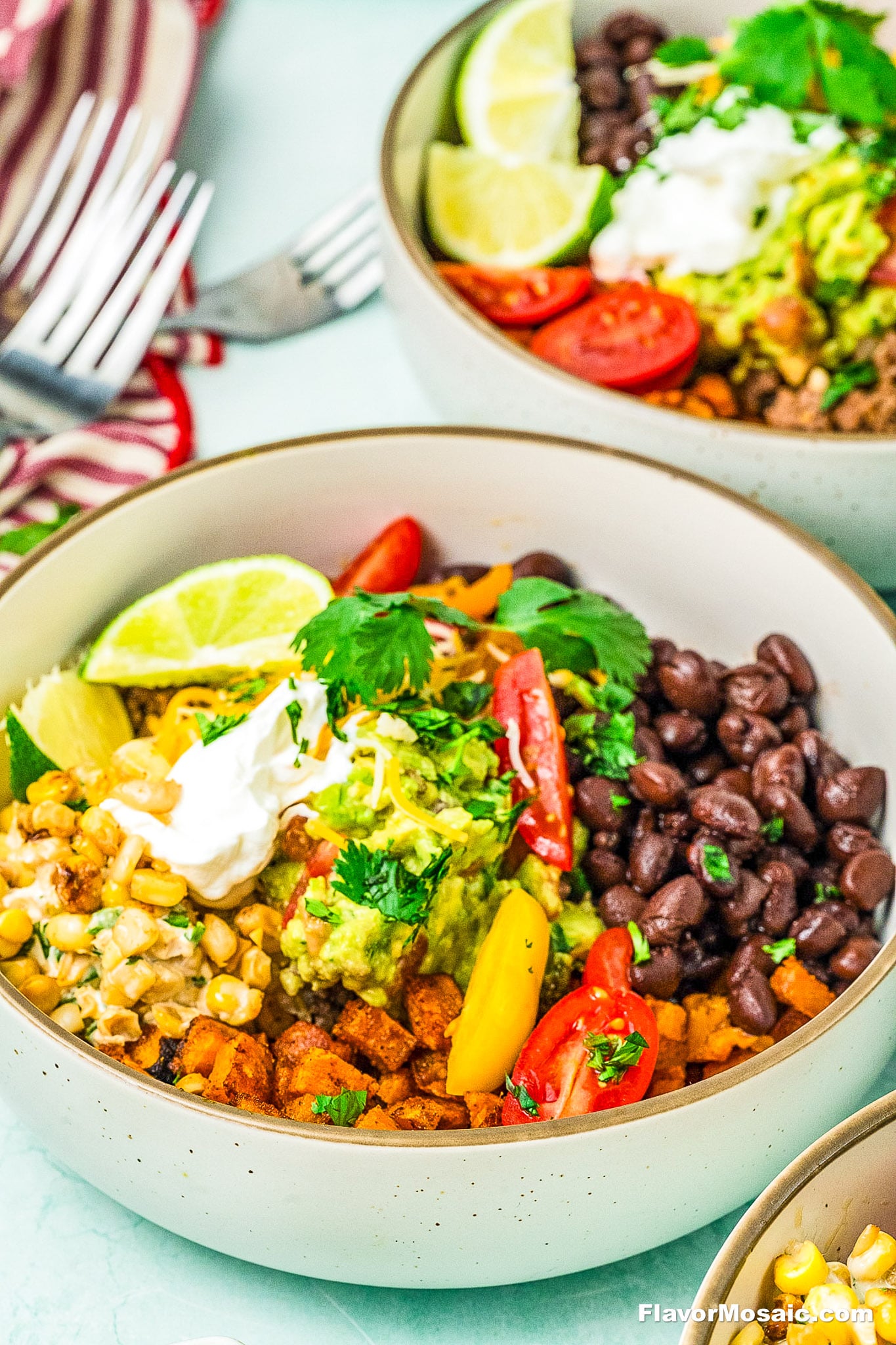 A colorful Ground Beef Sweet Potato Bowl with black beans, grilled corn, diced seasoned tofu, guacamole, cherry tomatoes, yellow peppers, lime wedges, fresh cilantro, and a dollop of sour cream in a light ceramic bowl.