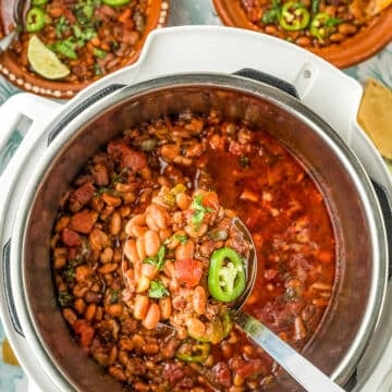 A close-up of a ladle lifting spicy pinto bean chili with jalapeño slices from an Instant Pot, surrounded by bowls of chili topped with cilantro and tortilla chips.