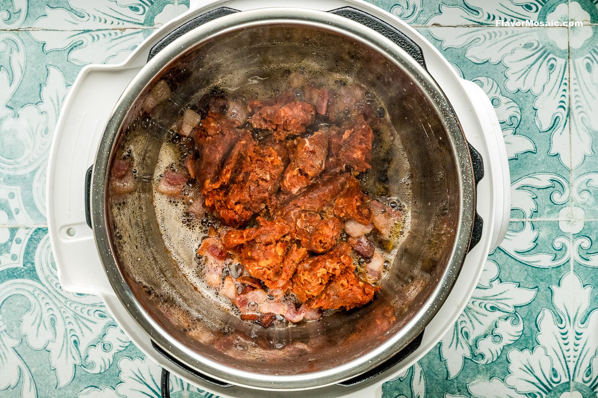 An overhead view of an Instant Pot with browned ground meat and onions cooking inside, perfect for starting Instant Pot Charro Beans (Frijoles Charros), set on a green and white patterned countertop as steam rises from the food.