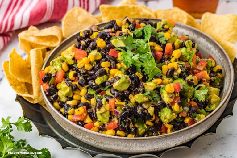 A bowl of black bean and corn salad with chopped tomatoes, avocado, and cilantro, surrounded by tortilla chips on a plate-a fresh and colorful addition to your favorite corn recipes.