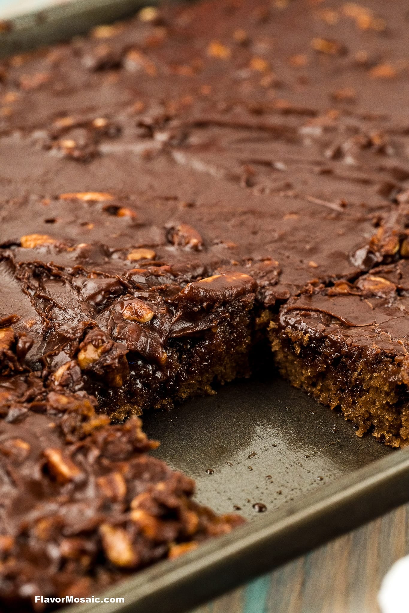 A close-up of a chocolate sheet cake in a pan with a slice removed, revealing its moist texture and chocolate frosting with nuts.