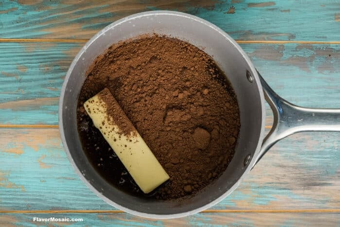A saucepan on a blue wooden surface contains a stick of butter and cocoa powder, ready to be mixed.