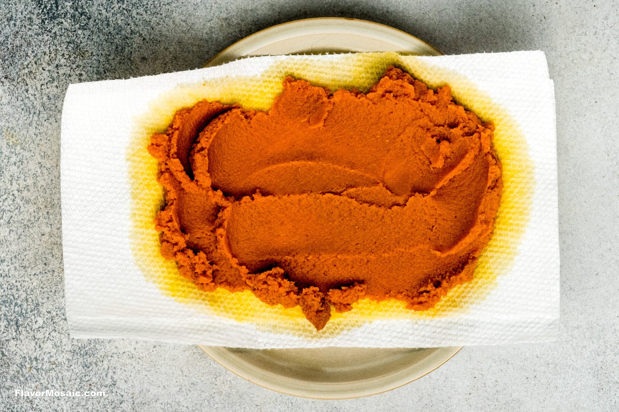 A mound of pumpkin spice pumpkin puree draining on a paper towel atop a plate.