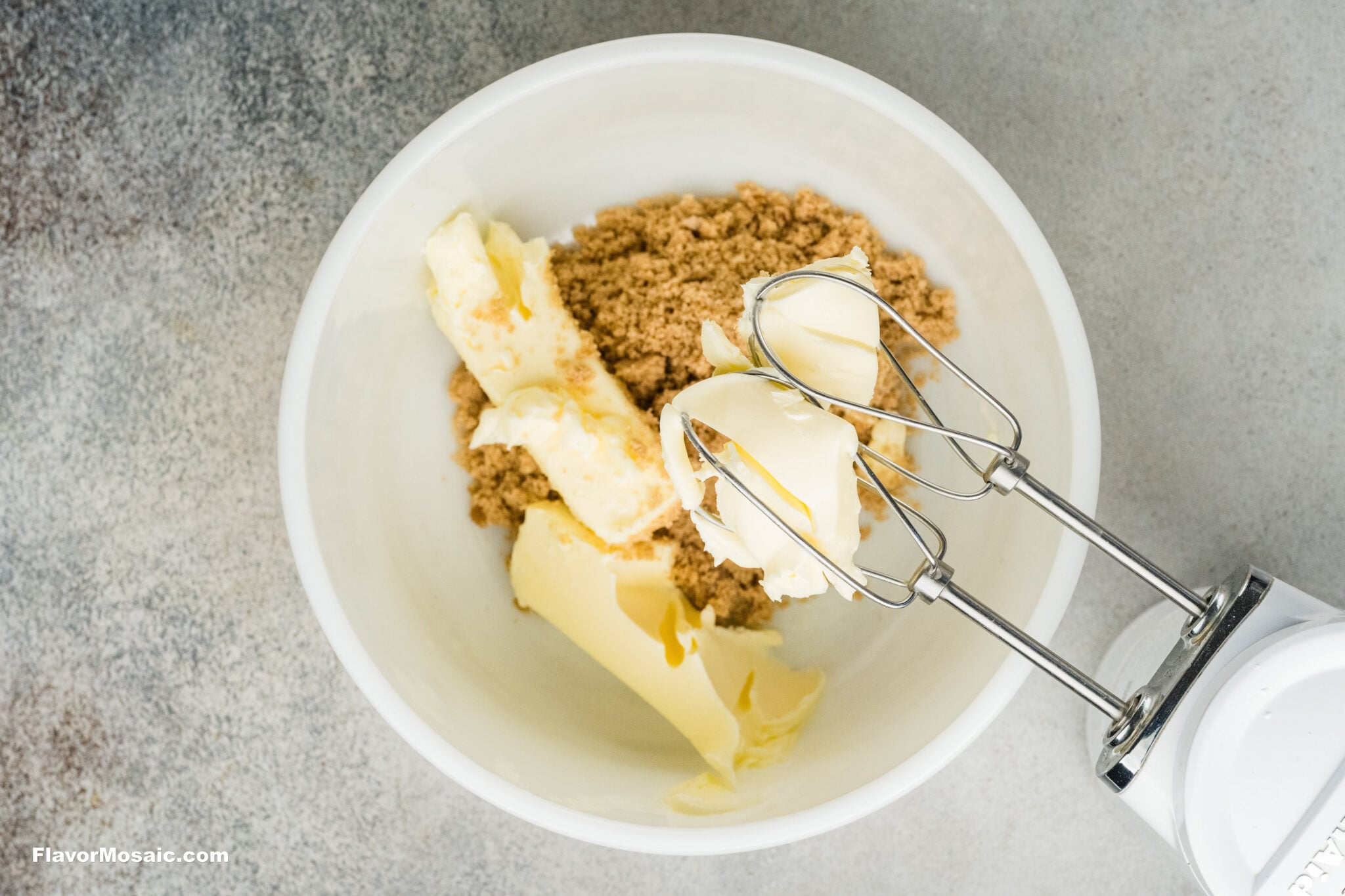 Handheld electric mixer beaters in a white bowl with butter and brown sugar for pumpkin spice sugar cookies.