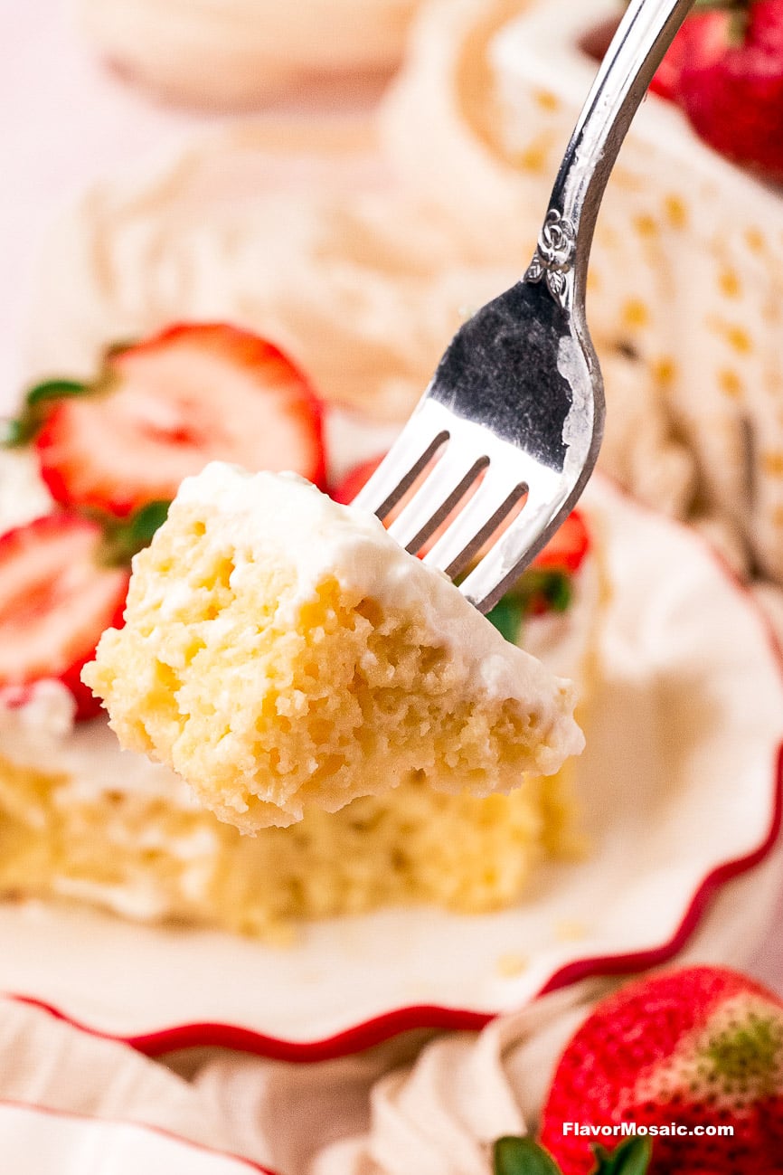 A silver fork holds a bite of tres leches cake topped with whipped cream, as seen in this dessert recipe.